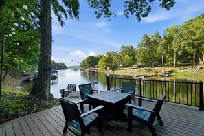 A deck with outdoor seating overlooking a calm river, surrounded by lush greenery and a clear sky. - 3 Story Waterfront Brick Home w Brand New Pool/Spa, foosball, ping pong and much more (Mooresville)