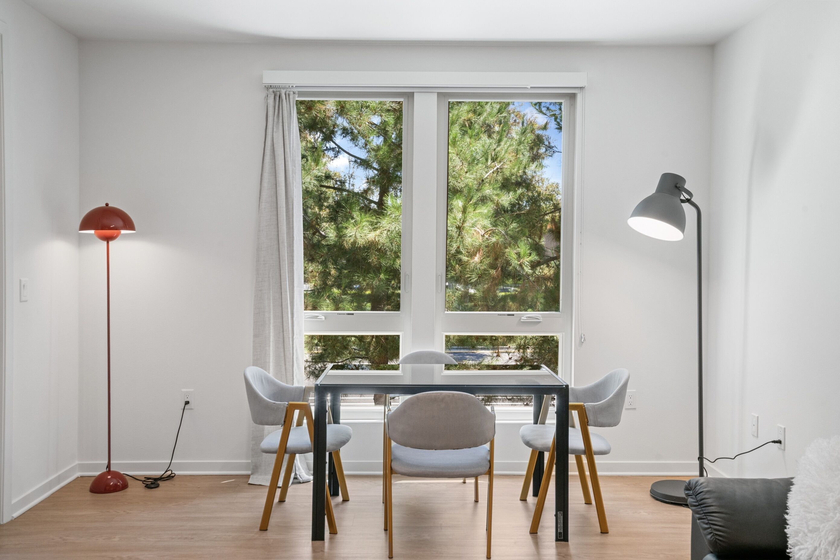 Een eetgedeelte met een tafel, stoelen, een rode vloerlamp en een zwarte vloerlamp.