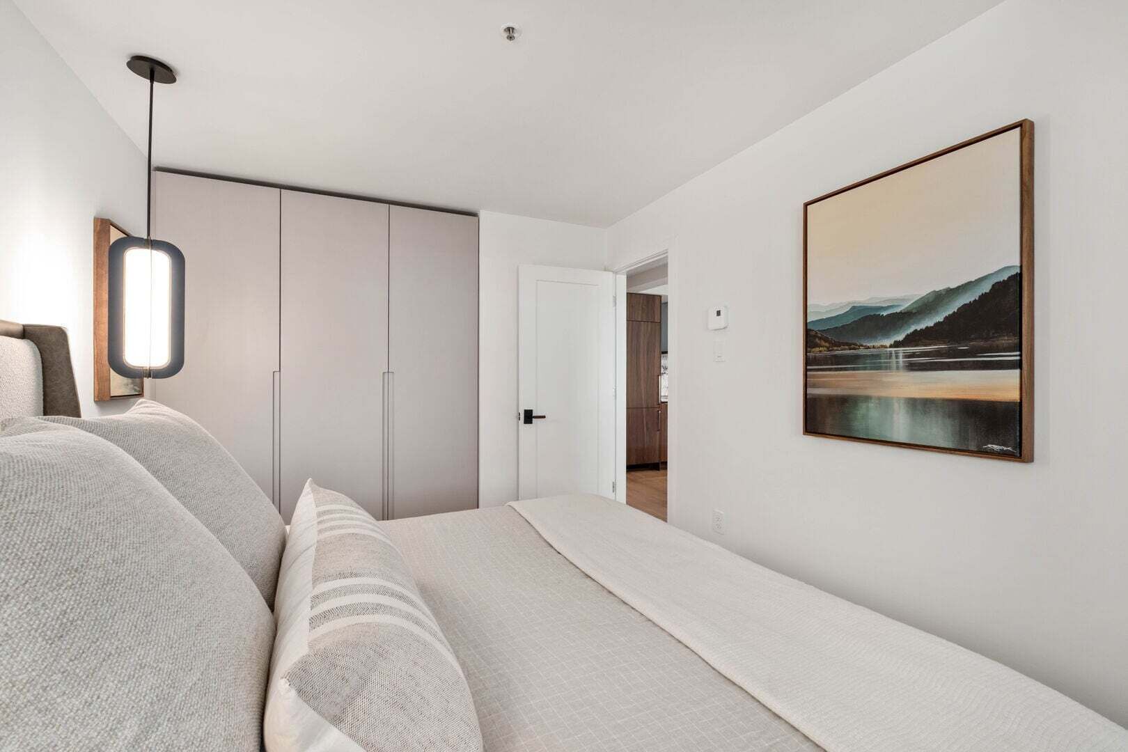 A bedroom with a bed, a wardrobe, a painting, and a pendant light.