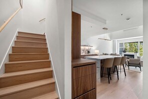 Eine moderne Küche mit einer zentralen Kochinsel, einer Holztreppe und einem Essbereich mit Barhocker.
