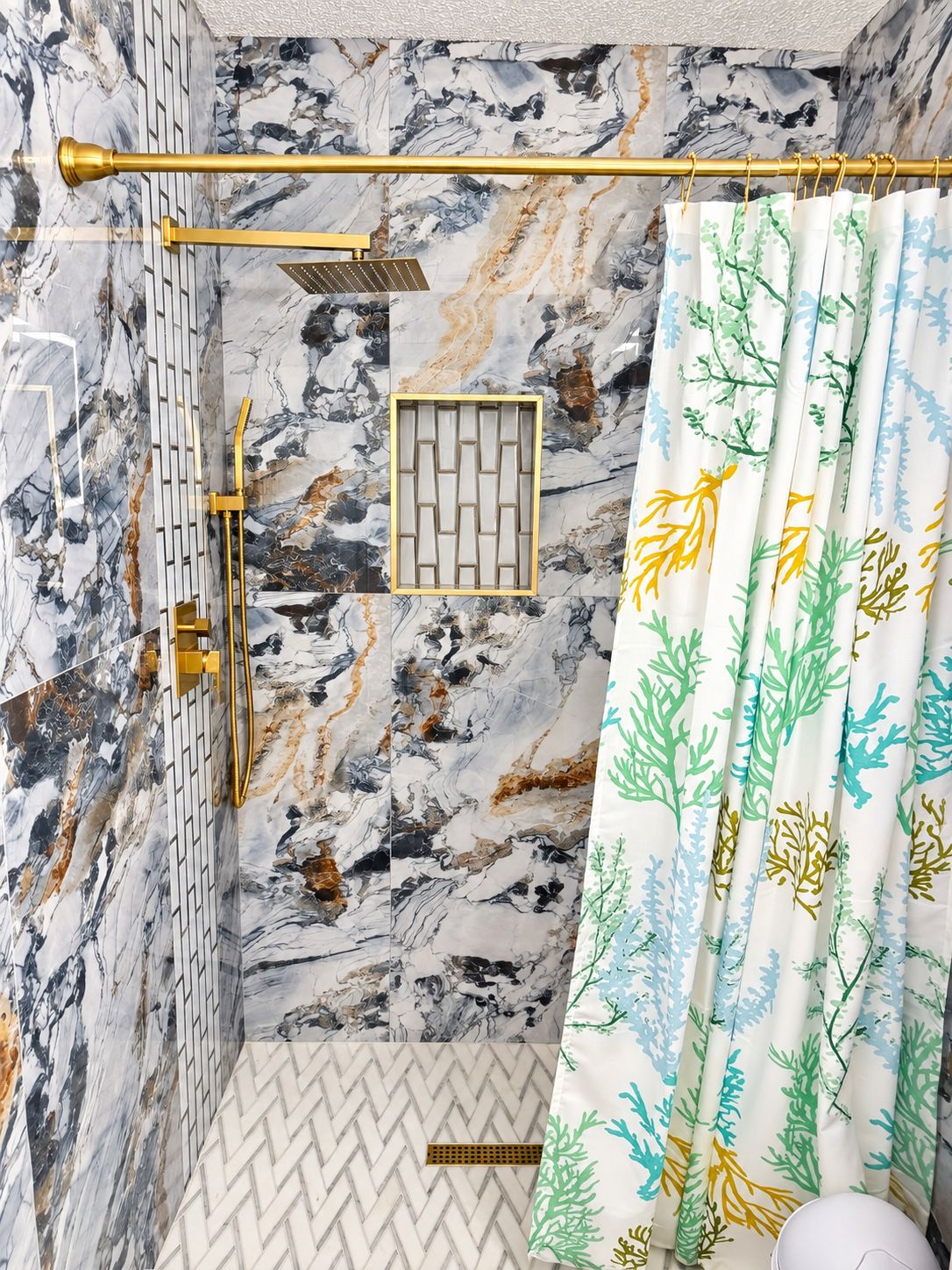 Ein Badezimmer mit Marmorwand, einer Dusche mit goldener Brause und einem Vorhang mit Blättermuster.