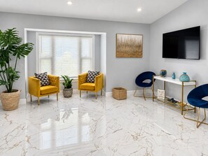 A modern living room with two yellow armchairs, a blue chair, a white console table, a large potted plant, and a flat-screen TV on the wall. - Enjoyable 3-bedroom house with pool and AC in charming Jacksonville, Florida. (Jacksonville)