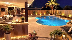 A swimming pool with a curved edge, surrounded by a wooden fence, and a covered patio area with seating and plants. - Enjoyable 3-bedroom house with pool and AC in charming Jacksonville, Florida. (Jacksonville)