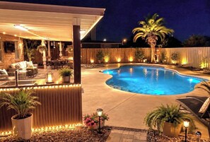 Ein Pool mit gewölbter Kante, umgeben von einem Holzzaun, und ein überdachter Patio-Bereich mit Sitzgelegenheiten und Pflanzen.