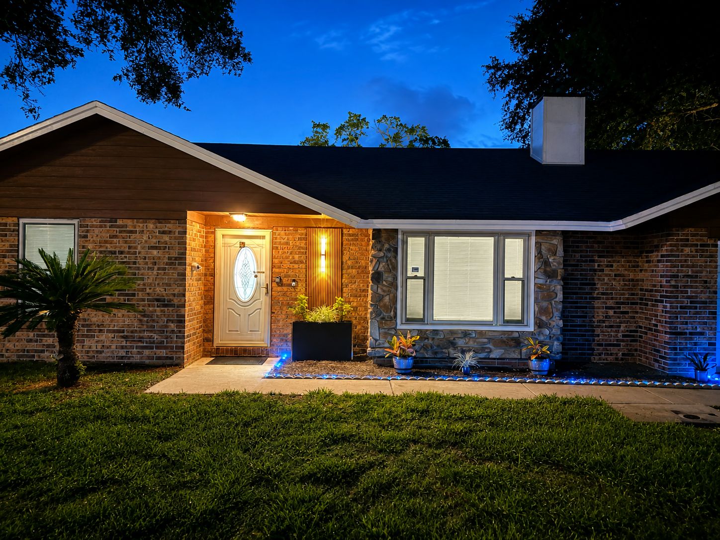 A residential house with a brick facade, a front door, and a small garden area with potted plants.