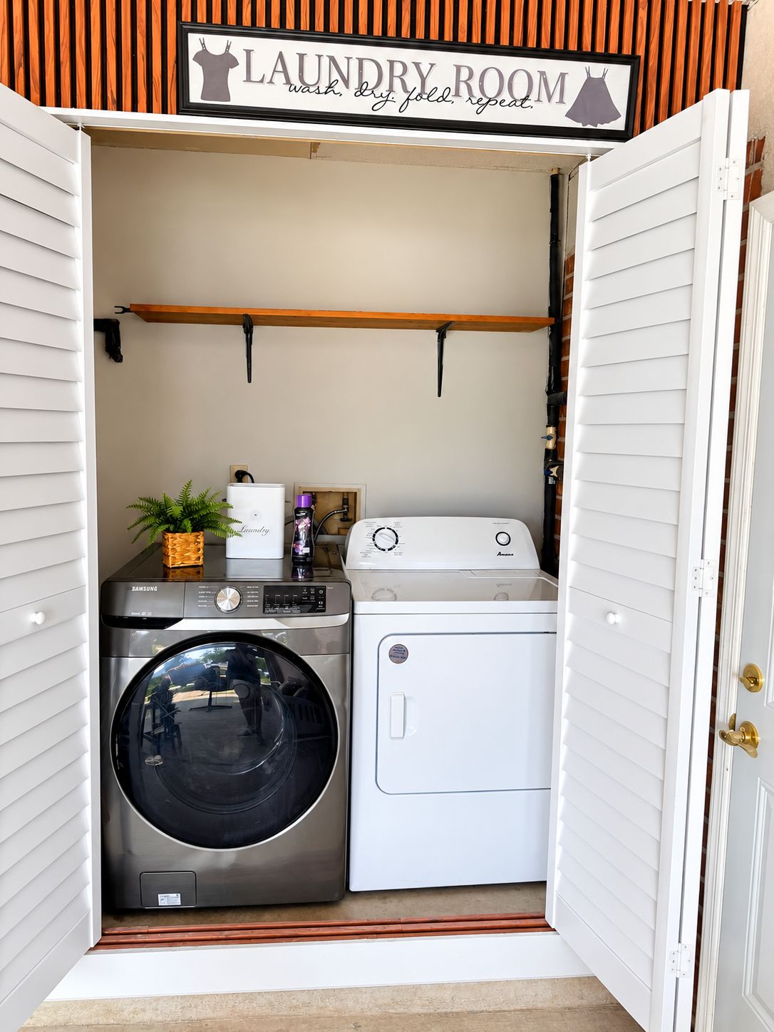Ein Waschraum mit einer Samsung Waschmaschine und einem Trockner, einem Regal darüber und einem Schild mit der Aufschrift 'LAUNDRY ROOM'.