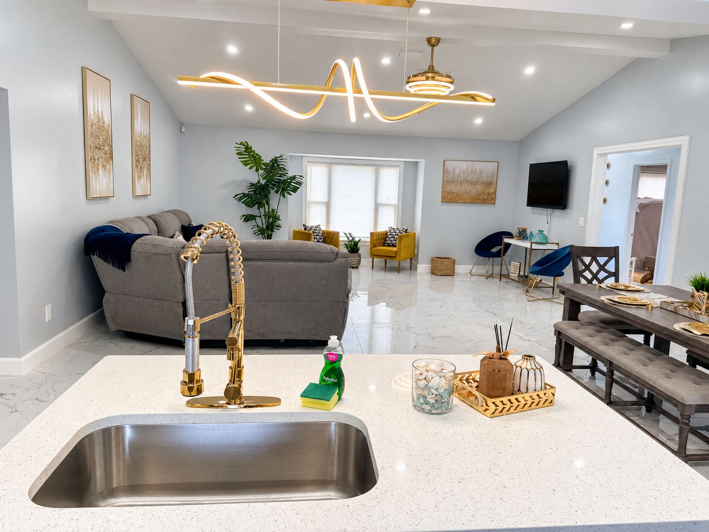 A modern kitchen with a stainless steel sink, a gold faucet, and a dining area with a marble countertop.