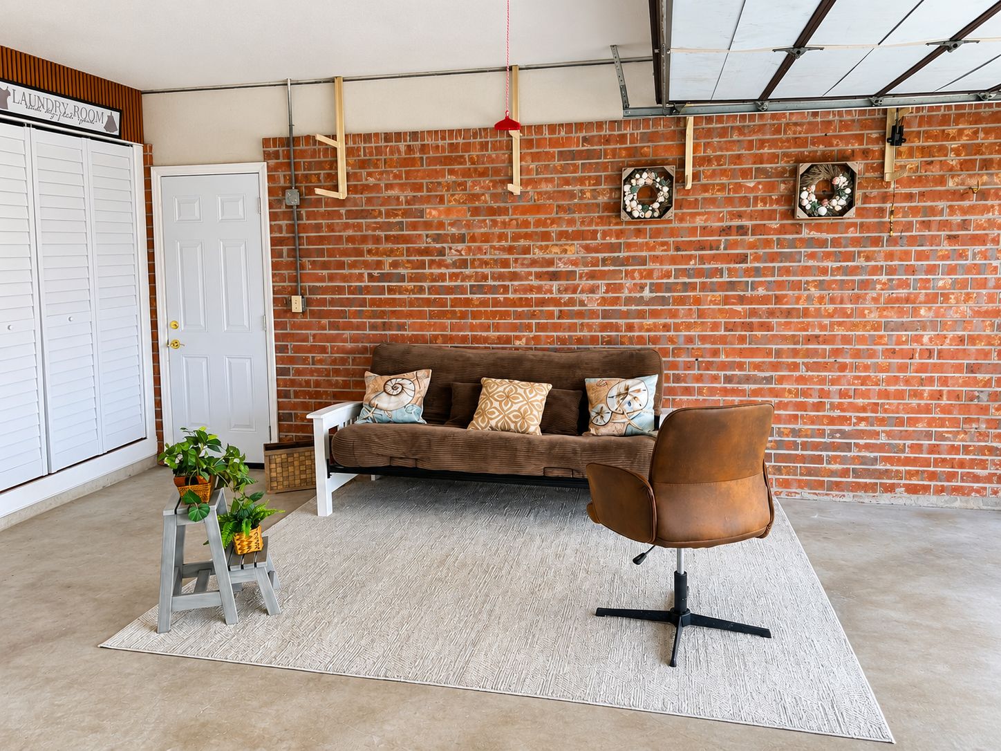 A room with a brick wall, a white door, a brown sofa, a brown chair, and a small plant.