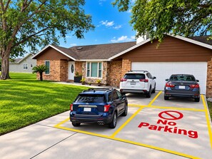 Une allée menant à une résidence, avec un panneau indiquant « Stationnement interdit », deux voitures garées et une maison avec un garage.
