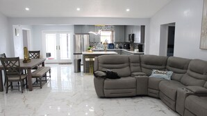 Een moderne woonkamer met een modulaire bank, een eettafel met stoelen en een keuken op de achtergrond.