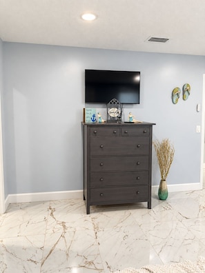 A room with a dark wooden dresser, a flat-screen TV mounted on the wall, and a vase with dried plants on the floor.