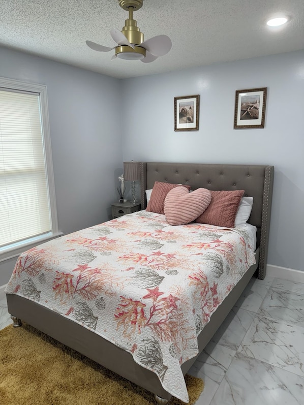 A bedroom with a bed, a nightstand, a lamp, and a ceiling fan.