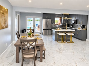 A modern kitchen with a central island, stainless steel appliances, and a dining area with a marble floor.
