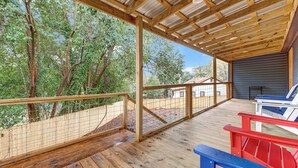 Une terrasse en bois couverte, dotée d’une rambarde en métal, et entourée d’arbres.