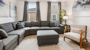 Una sala de estar moderna con un sofá modular, un reposapiés, un sillón de madera y una mesita de noche con una lámpara.