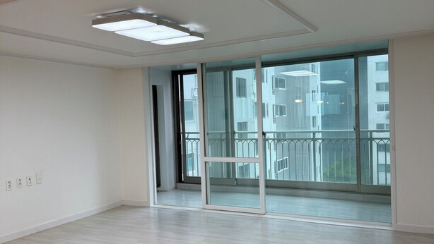 A spacious room with a large sliding glass door leading to a balcony, a ceiling light fixture, and a clean, light-colored wooden floor. - Happy house (Yongin-si)