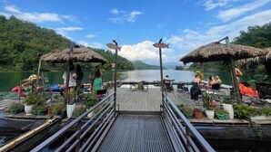 Une jetée en bois, agrémentée de parasols en chaume, de plantes en pot et offrant une vue sur un lac.