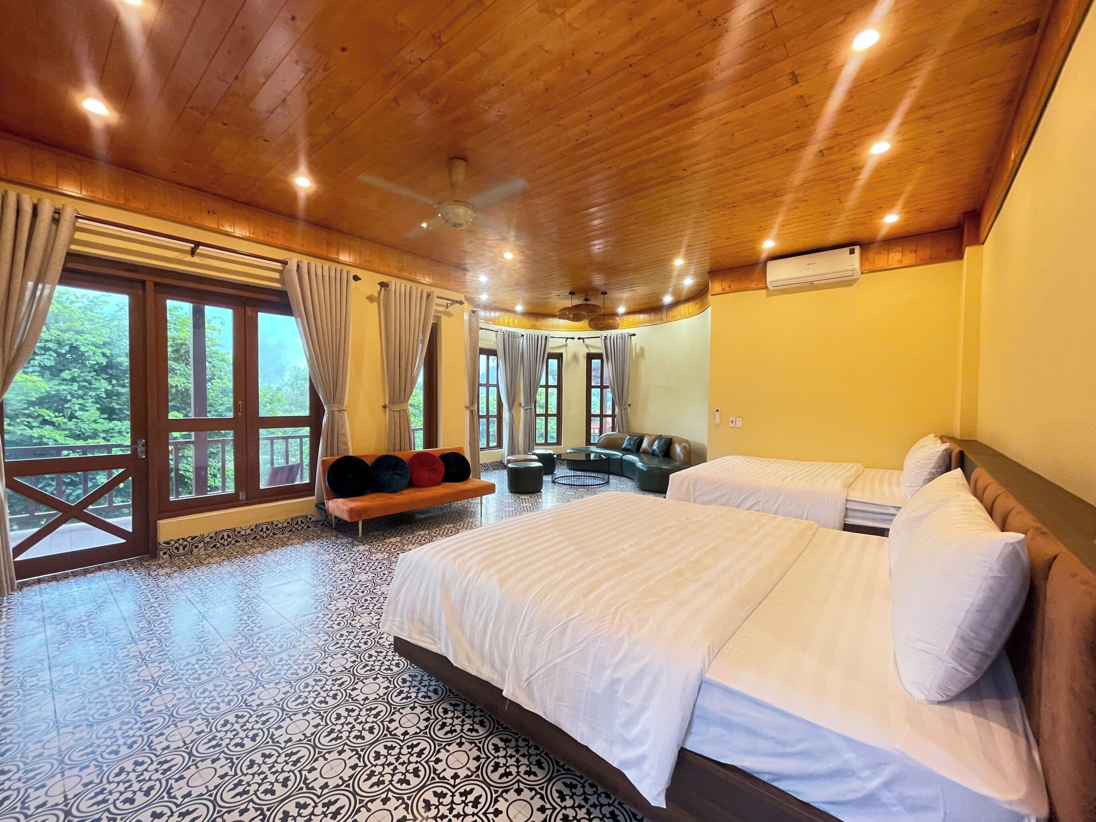 A room with two beds, a sofa, a coffee table, and large windows with curtains.