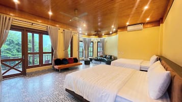 Quarto com duas camas, um sofá, uma mesa de centro e janelas amplas com cortinas.