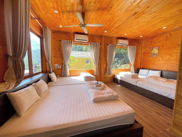 Dormitorio de cabaña de madera con dos camas, un ventilador de techo y ventanas grandes con cortinas.