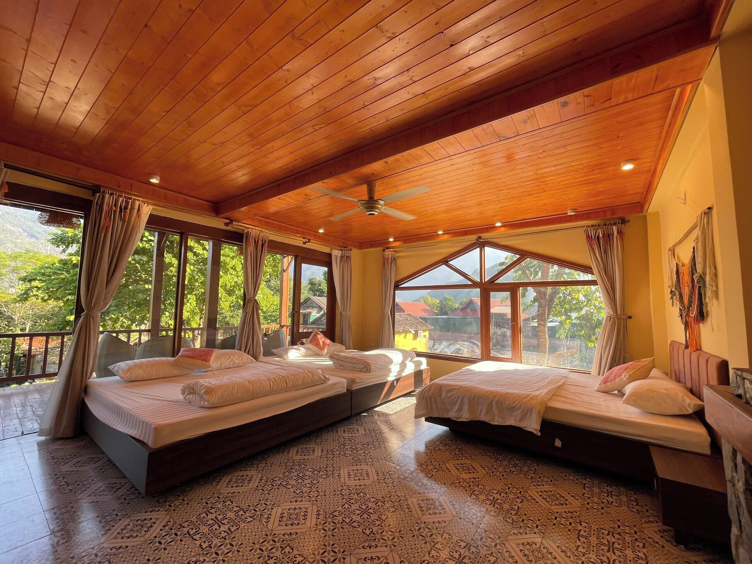 A room with two beds, large windows, a wooden ceiling, and patterned floor tiles.