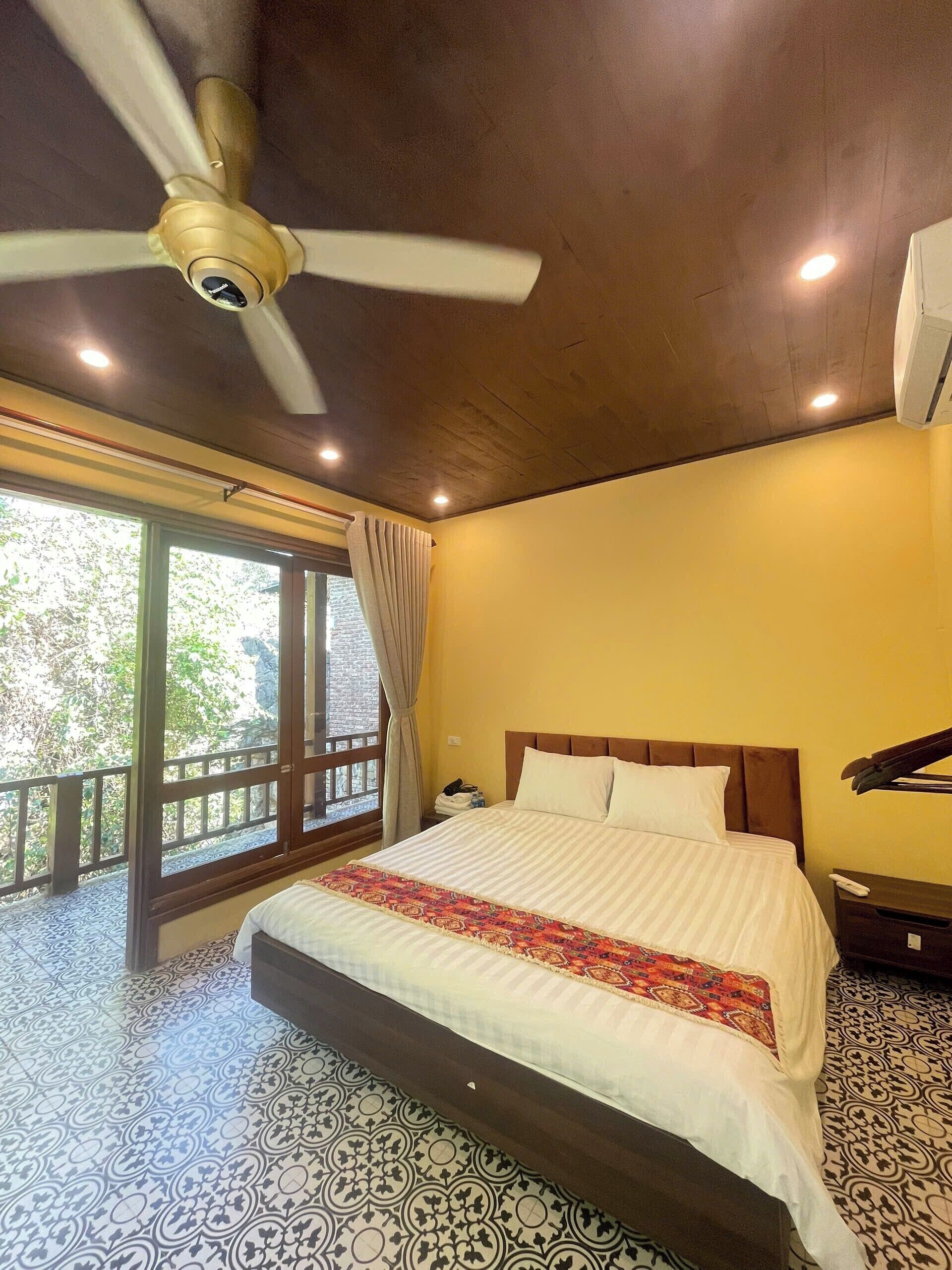 Una camera d'hotel con un letto grande, una ventola a soffitto, un balcone con vista e un pavimento decorato.