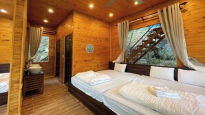 Une chambre dans une cabane en bois, avec deux lits, un ventilateur de plafond et une fenêtre avec des rideaux.