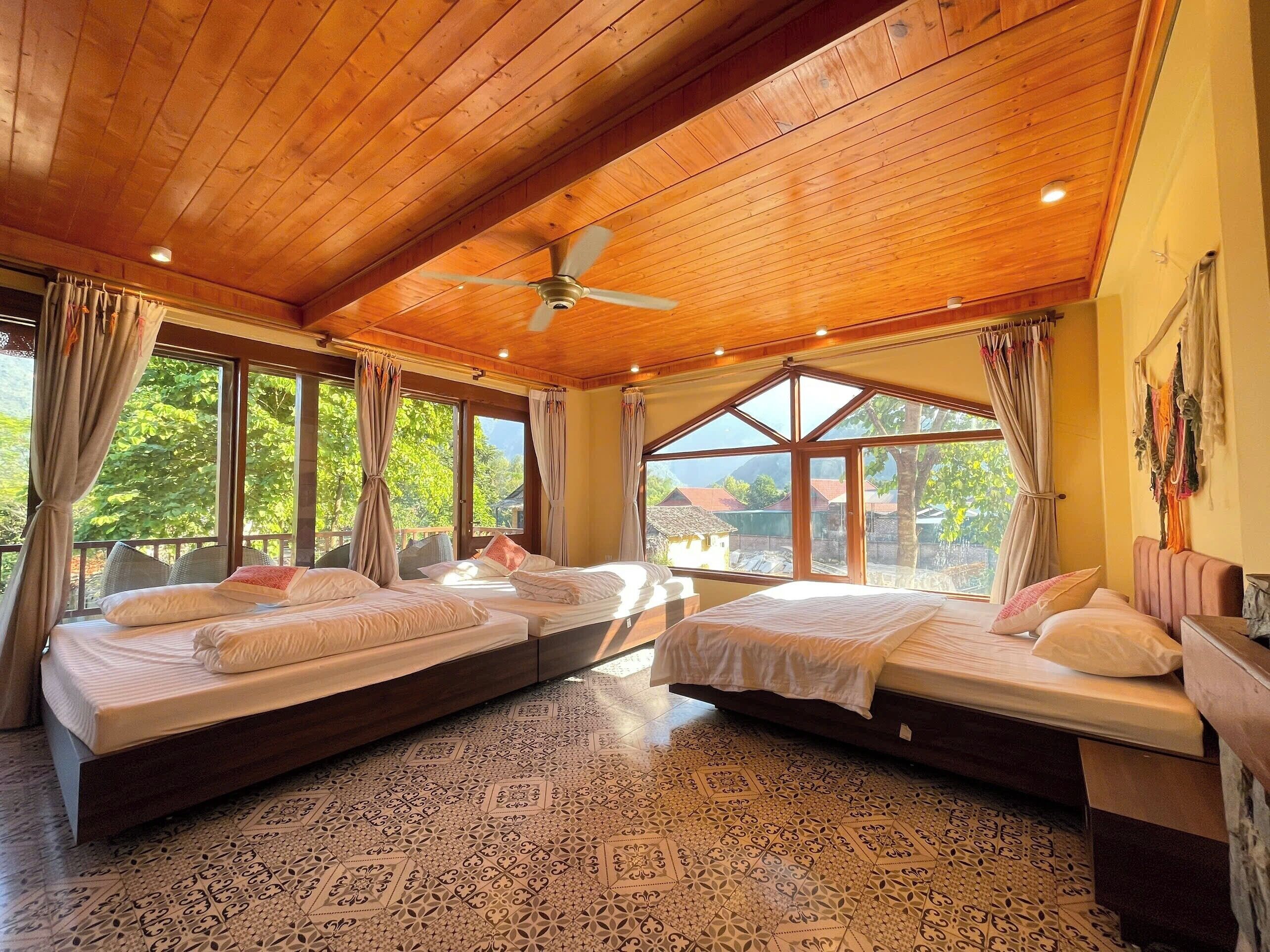 Una habitación con dos camas, ventanas amplias, un ventilador de techo y baldosas de suelo estampadas.