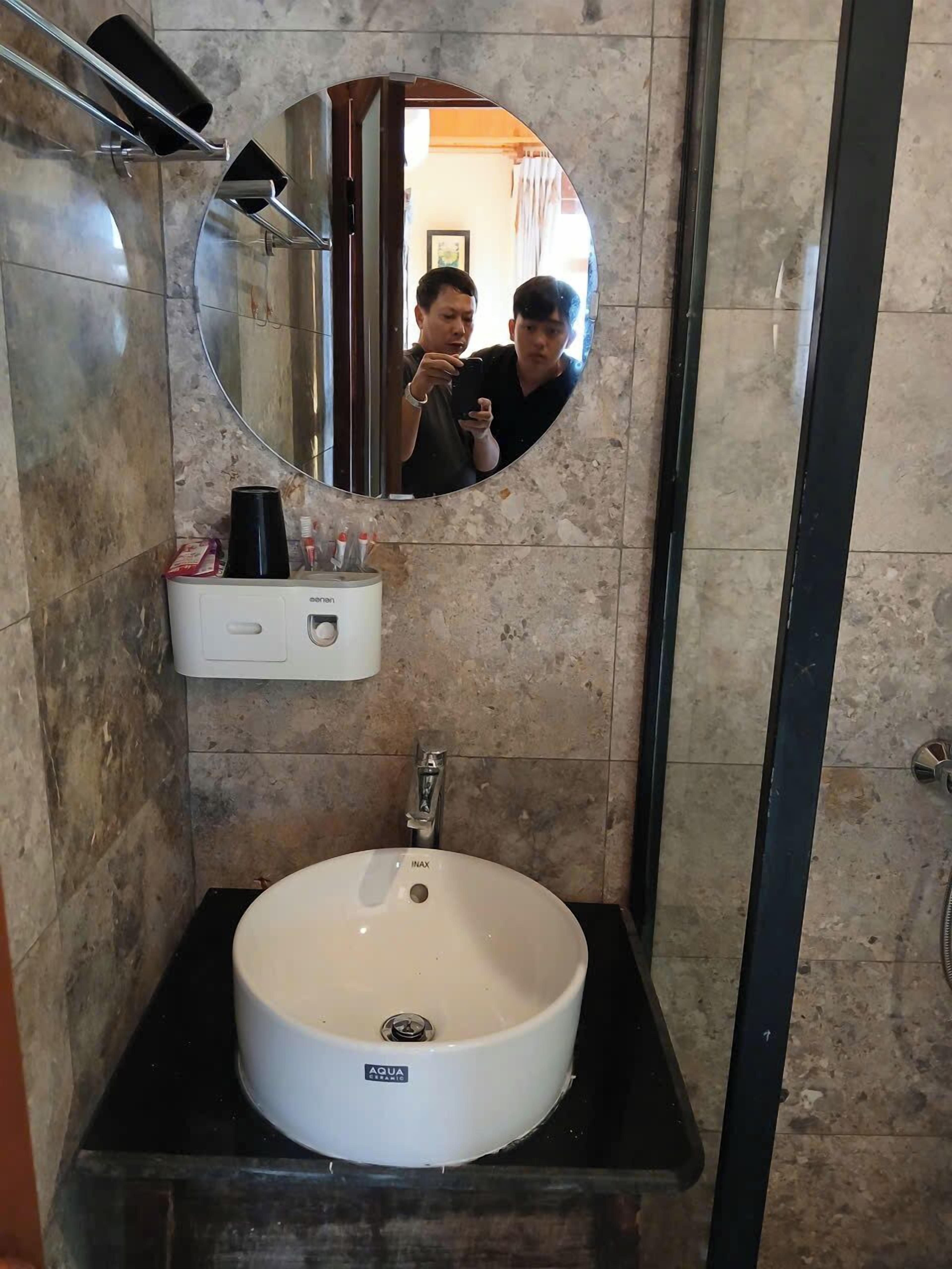 A bathroom with a round mirror, a white sink, and a black countertop.