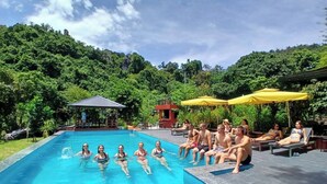 Une piscine entourée d’une végétation luxuriante, où des gens se détendent et prennent des bains de soleil.