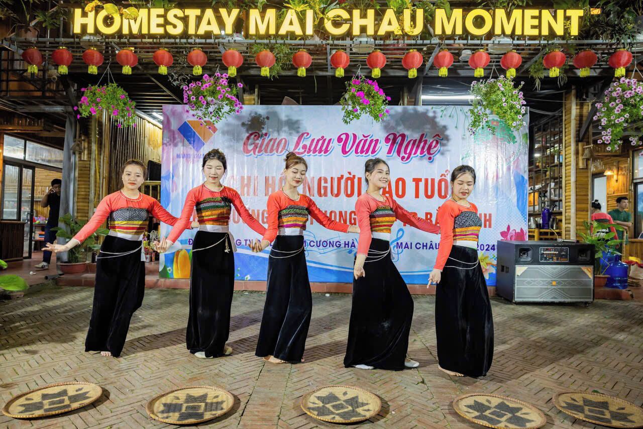 A group of women performing a traditional dance in front of a banner with text and decorations.