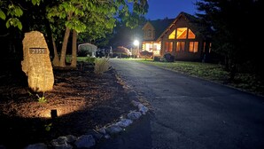 Een nachtzicht van een huis met een verlichte veranda, een stenen bordje met '2355' erop, en een verharde oprit naar de ingang.
