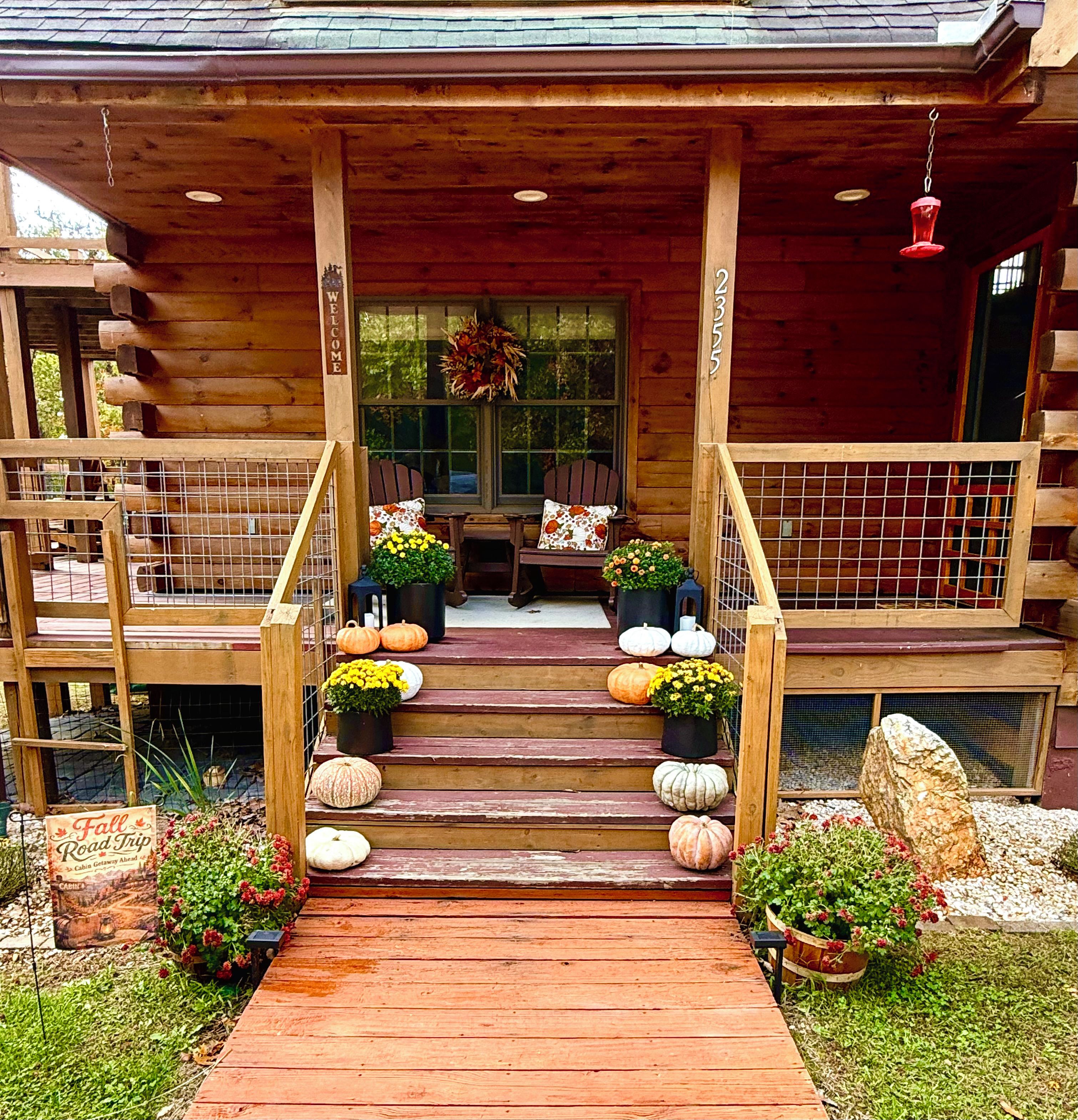 A wooden cabin with a porch, a welcome sign, and a sign indicating a fall road trip.
