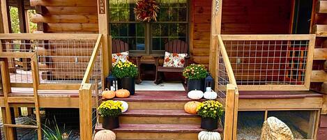 A wooden cabin with a porch, a welcome sign, and a sign indicating a fall road trip.
