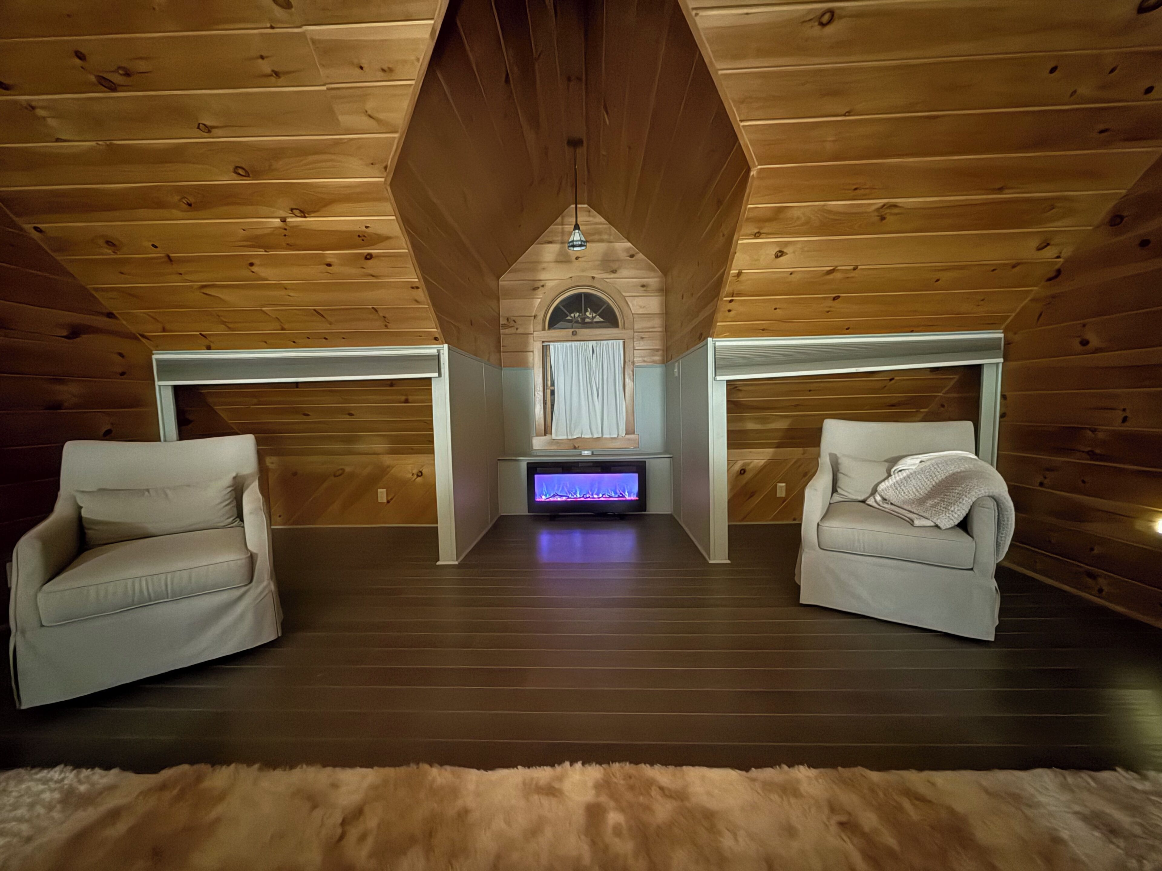 A room with wooden ceiling, two sofas, a fireplace, and a TV.