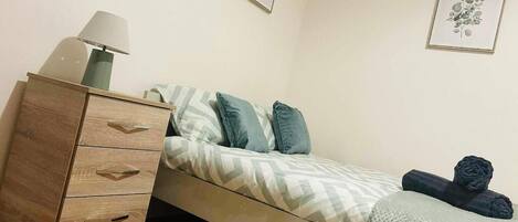 A bedroom with a bed, a wooden dresser, a lamp, and two framed pictures on the wall.