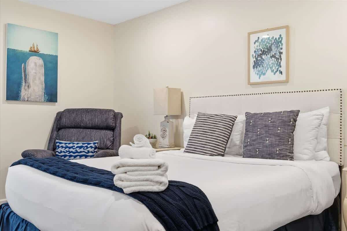 Una habitación de hotel con cama, una silla, una lámpara y obras de arte en las paredes.