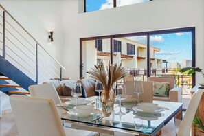 Ein moderner Essbereich mit einem Glastisch, weißen Stühlen und einer dekorativen Vase. Eine Treppe ist links zu sehen, und im Hintergrund ein Balkon mit Blick auf Gebäude.