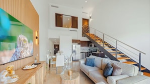 Un salon moderne avec un canapé, une table basse et un téléviseur fixé sur un mur en bois. Un escalier avec une rampe mène à un niveau supérieur.