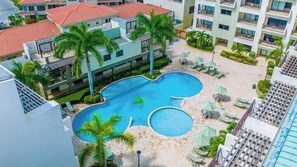 Un hotel con piscina centrale circondata da lettini e palme.