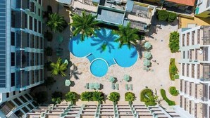 Une piscine sur le toit, entourée de palmiers et de chaises longues, avec des bâtiments modernes en arrière-plan.