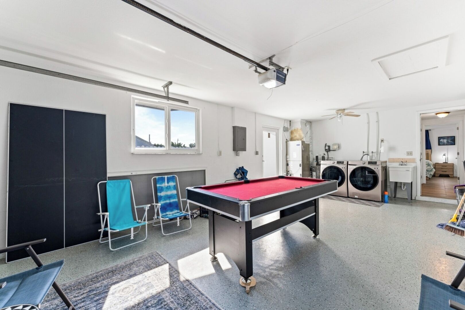 A pool table in a room with a washing machine and a small kitchenette.