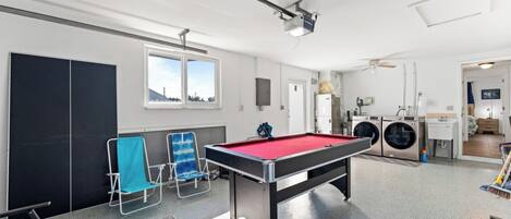 A pool table in a room with a washing machine and a small kitchenette.