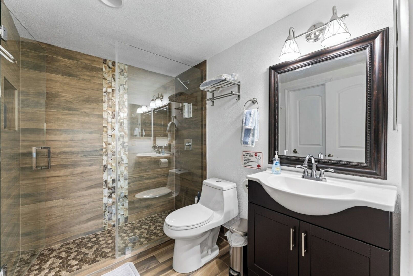 Une salle de bain moderne avec une douche à parois de verre, des toilettes blanches, un meuble-lavabo avec un grand miroir et un évier.