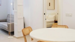 Een kamer met een ronde tafel, twee houten stoelen, een grijze bank en een witte fauteuil.