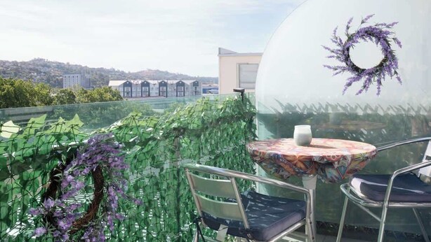 A glass-enclosed balcony with a table and chairs, a decorative wreath, and a view of buildings in the distance. - CBD Apartment - Walk to Shops & Attractions (Launceston)