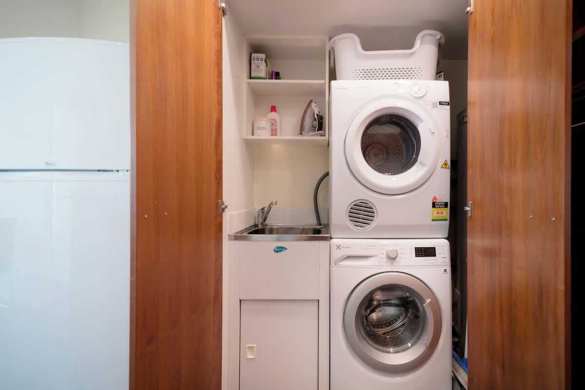 Un espace buanderie compact comprenant un lave-linge, un sèche-linge et une étagère où sont rangés les produits de nettoyage.