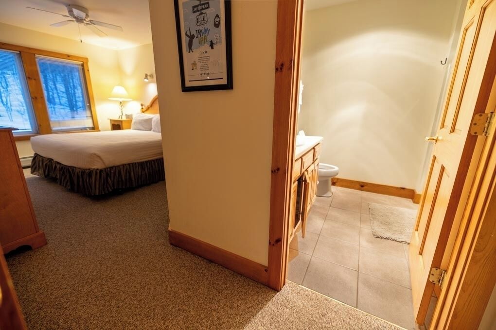 A hotel room with a bed, a desk, a chair, a window, and a door.