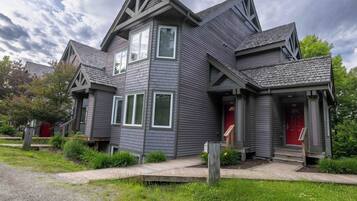 Une maison à deux étages avec une porte rouge, un porche à l’avant et un jardin bien entretenu.