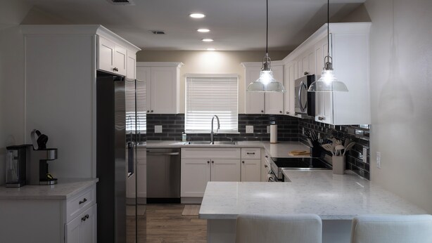 Una cocina moderna con armarios blancos, un refrigerador de acero inoxidable, una isla central con taburetes y luces colgantes.